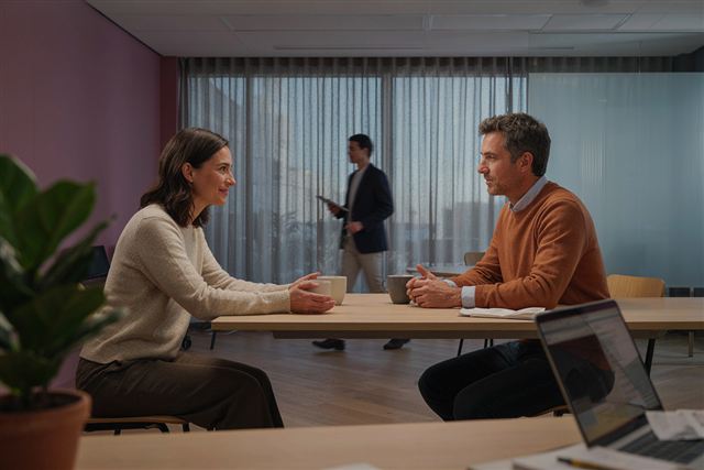 Dois colegas de trabalho conversando numa sala de reunião, em clima amigável.